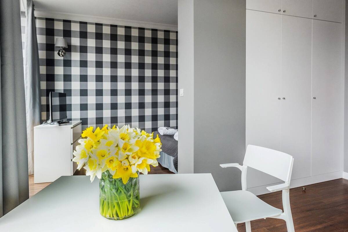 Une chambre moderne avec une table blanche, un vase de fleurs jaunes, un mur à carreaux et une armoire blanche.
