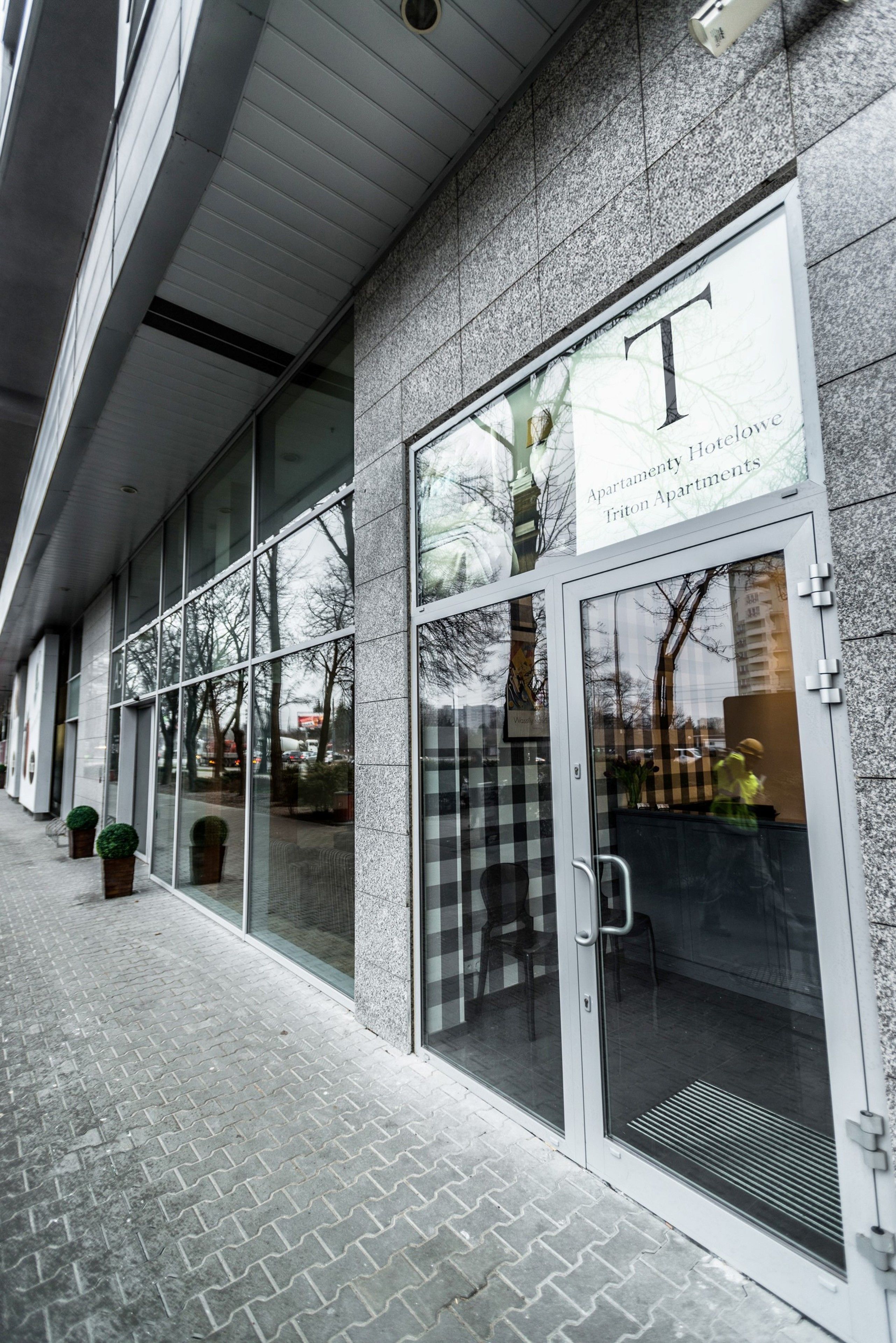 A modern building with a large glass facade, a prominent 'T' logo, and a sign for 'Apartment House Iratone Apartments'.