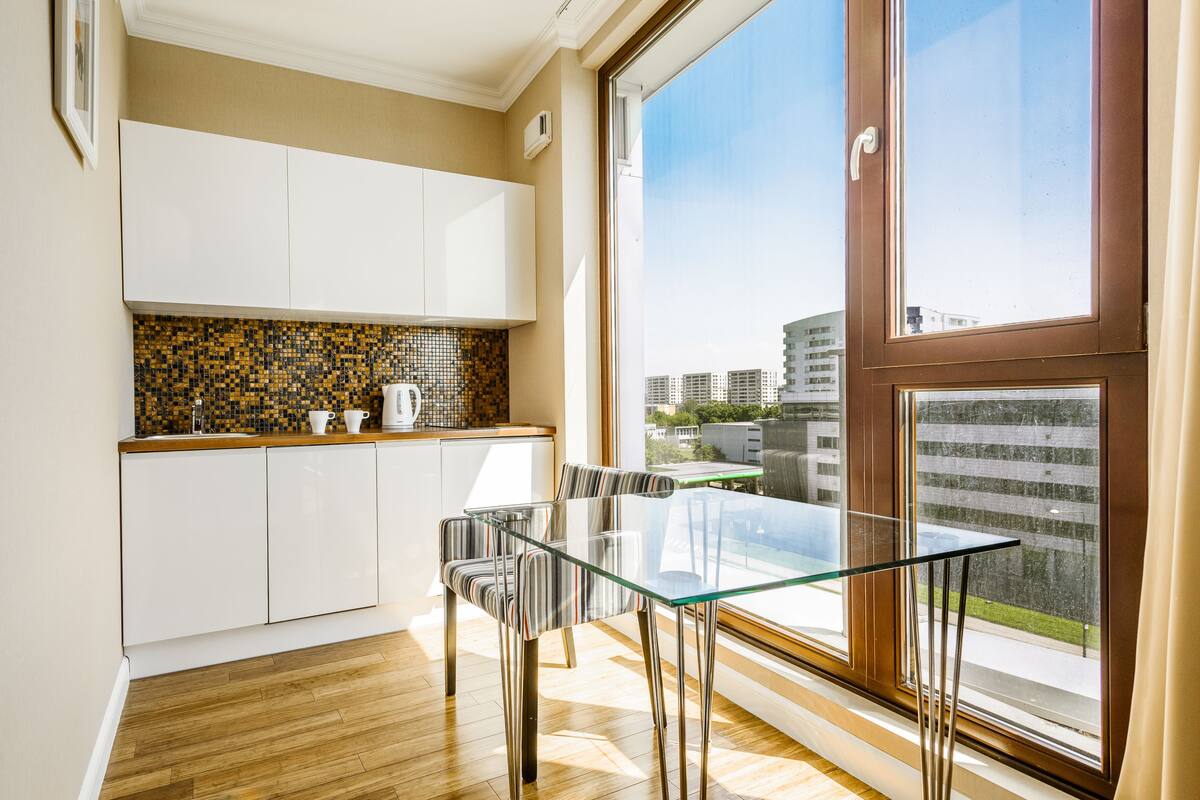 Une cuisine moderne avec des meubles blancs, un pare-feu en carreaux et un coin repas comprenant une table en verre et des chaises à rayures.