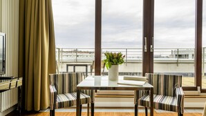 Une pièce moderne avec une grande fenêtre, une table, deux chaises à rayures, une plante en pot et un radiateur.