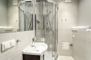 A modern bathroom with a glass-enclosed shower, a white sink, and neatly folded towels. - Triton Park Apartments (Warsaw)