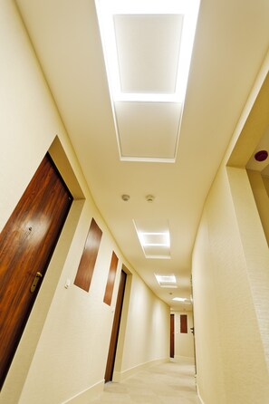 A corridor with a wooden door on the left, a ceiling with recessed lighting, and a carpeted floor. - Triton Park Apartments (Warsaw)