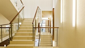 Un escalier moderne avec des rampes en verre et des mains courantes en bois, menant à l’étage supérieur.