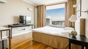Une chambre d’hôtel avec un lit, un bureau avec une télévision, une fenêtre donnant sur la ville et une lampe sur une table de chevet.