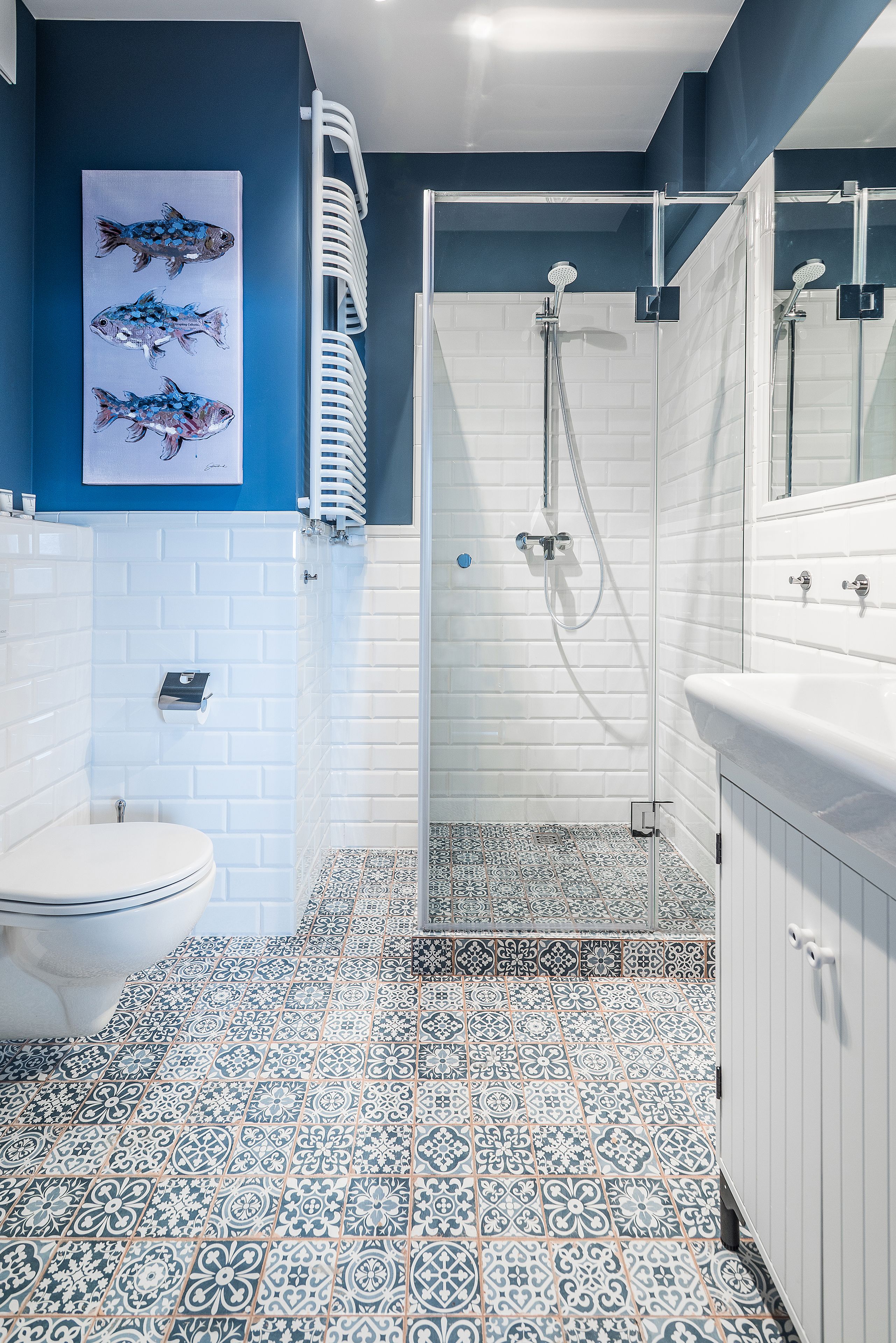A bathroom with a white toilet, a glass-enclosed shower, and a tiled floor with a blue and white pattern.
