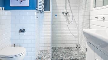 A bathroom with a white toilet, a glass-enclosed shower, and a tiled floor with a blue and white pattern.
