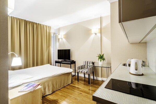 Habitación de hotel con cama, escritorio, silla, televisor, tetera y una mesita con una planta.