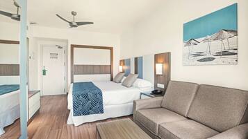 A hotel room with a bed, a sofa, a desk, a nightstand, a painting, a ceiling fan, and a door.