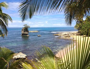 A tropical beach with clear blue water, rocky outcrops, and palm trees. - Physis Caribbean Bed & Breakfast (Cahuita)
