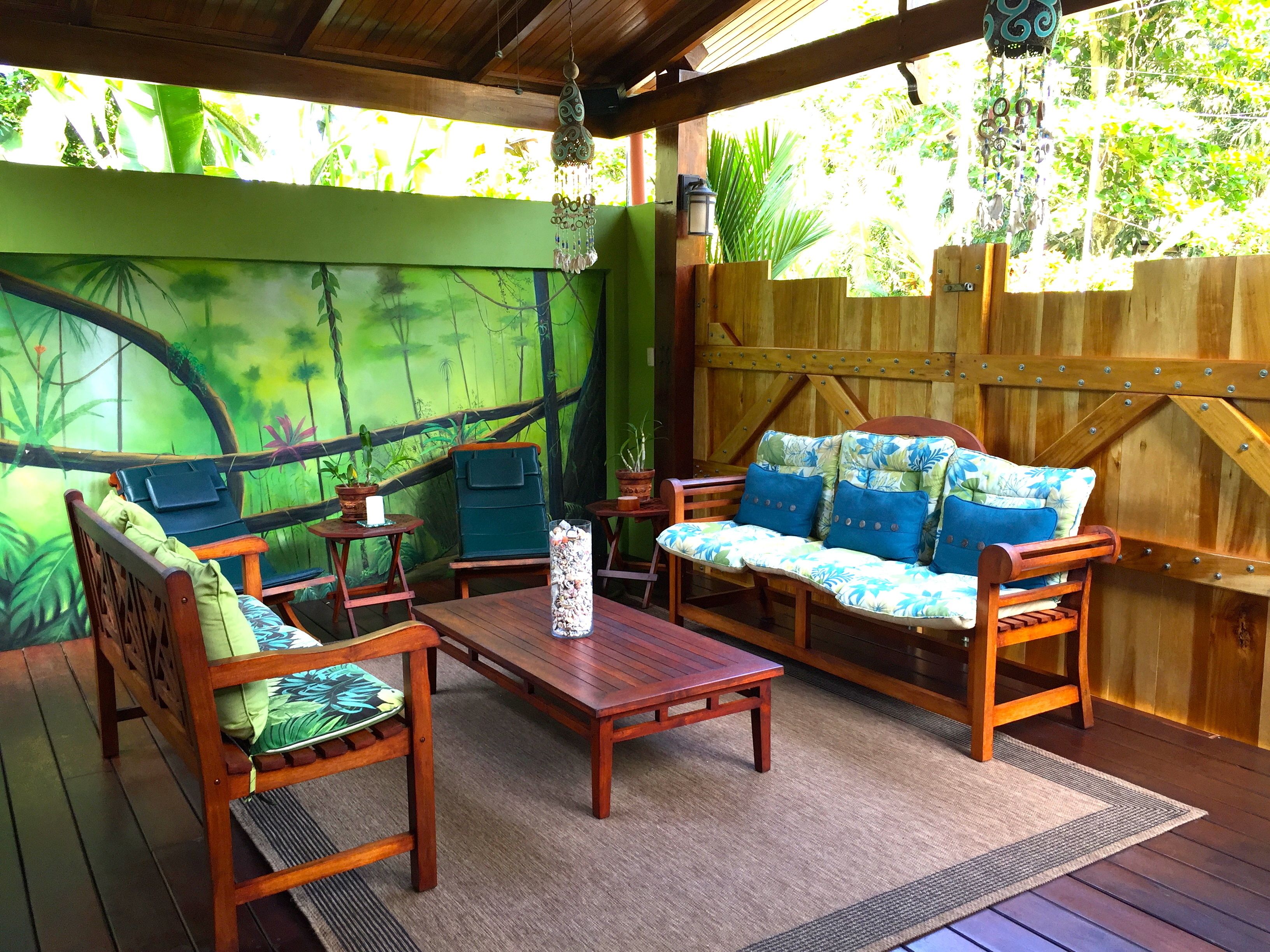 An outdoor patio with wooden furniture, a mural of a forest, and a wooden fence.