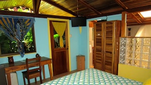 A bedroom with a bed, a desk, a chair, a wardrobe, and a television. - Physis Caribbean Bed & Breakfast (Cahuita)
