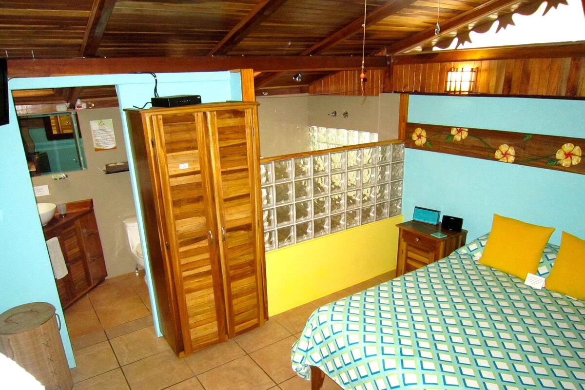 Une chambre à coucher comprenant un lit, une armoire en bois et une salle de bain avec des toilettes et un lavabo.