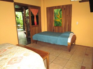 A room with two beds, wooden walls, a tiled floor, and a door leading outside.