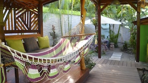A hammock under a wooden pergola, a wooden bench with cushions, and a garden with plants and a stone wall. - Physis Caribbean Bed & Breakfast (Cahuita)