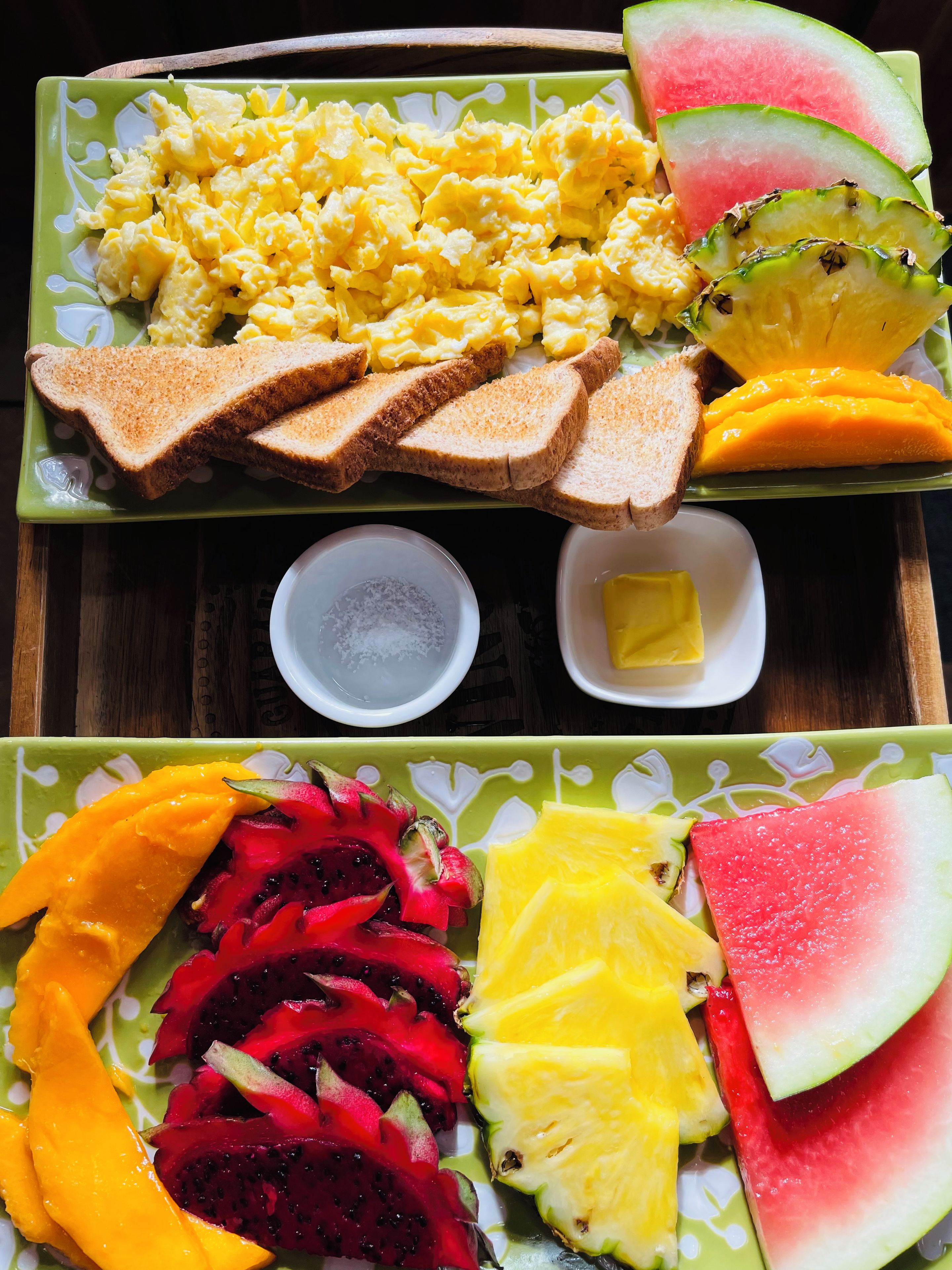 A tray with scrambled eggs, toast, and various fruits including mango, dragon fruit, pineapple, and watermelon.