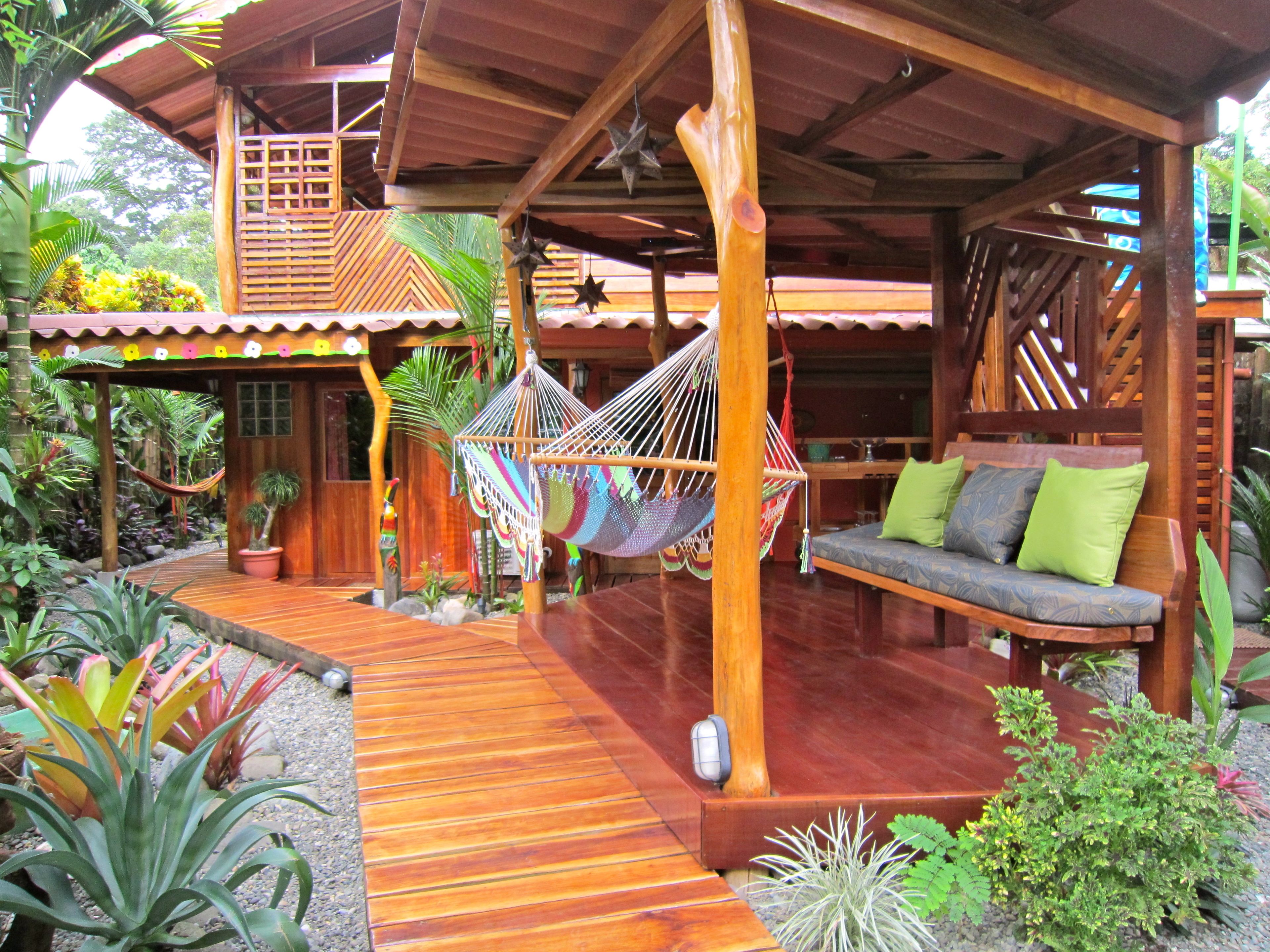 Una estructura de madera con una hamaca, un banco de madera con cojines y una terraza de madera.