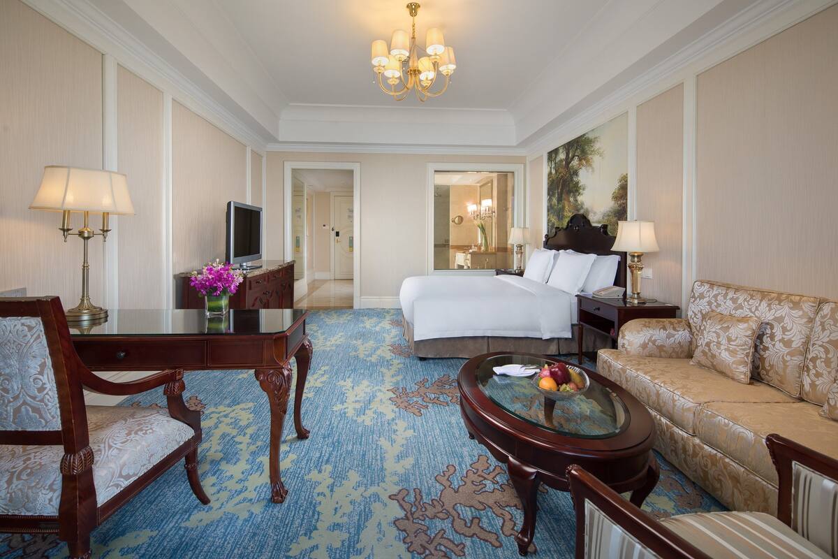 A hotel room with a bed, a sofa, a desk with a lamp, a chair, and a coffee table.