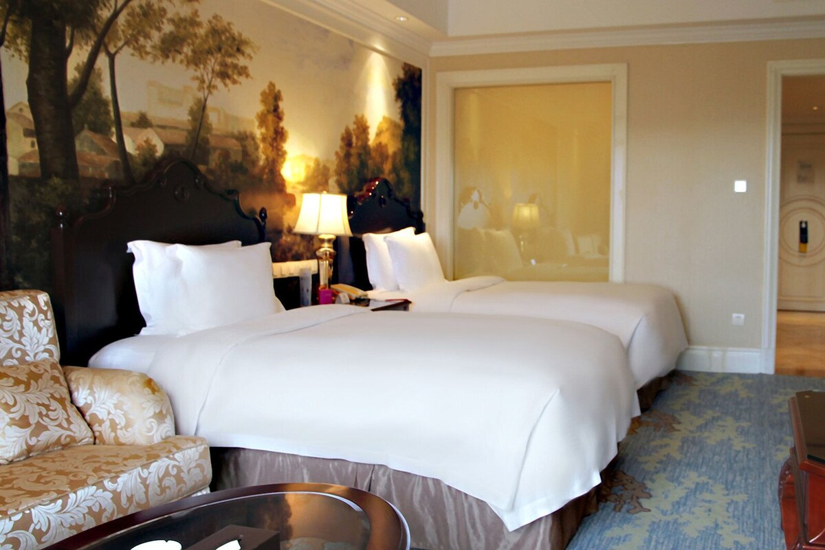 A hotel room with a bed, two bedside tables, a lamp, a television, a desk, and a chair.