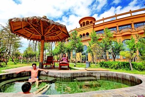 A swimming pool with a wooden canopy, a building with balconies, and a lush green garden. - Crowne Plaza Qingdao Ocean Spring Resort by IHG (Qingdao)