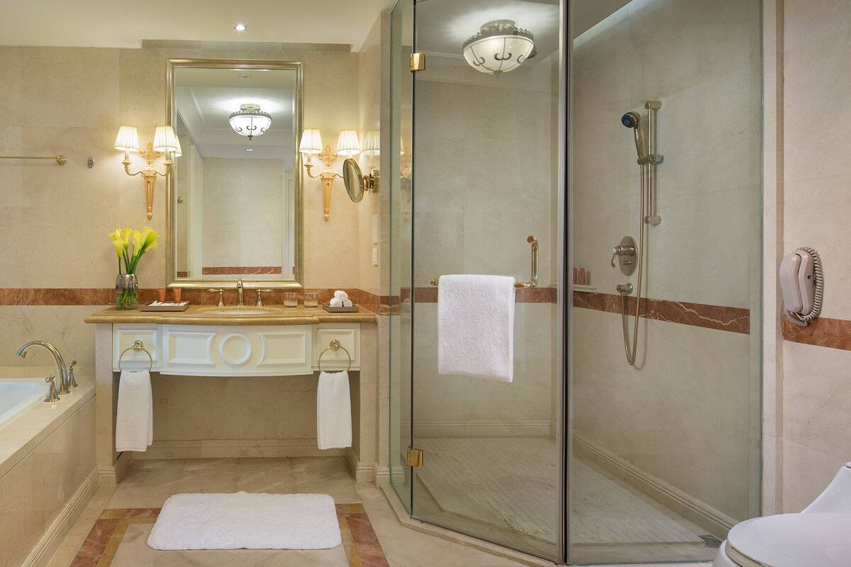 A bathroom with a bathtub, a glass-enclosed shower, a vanity with a mirror, and a vase of flowers.