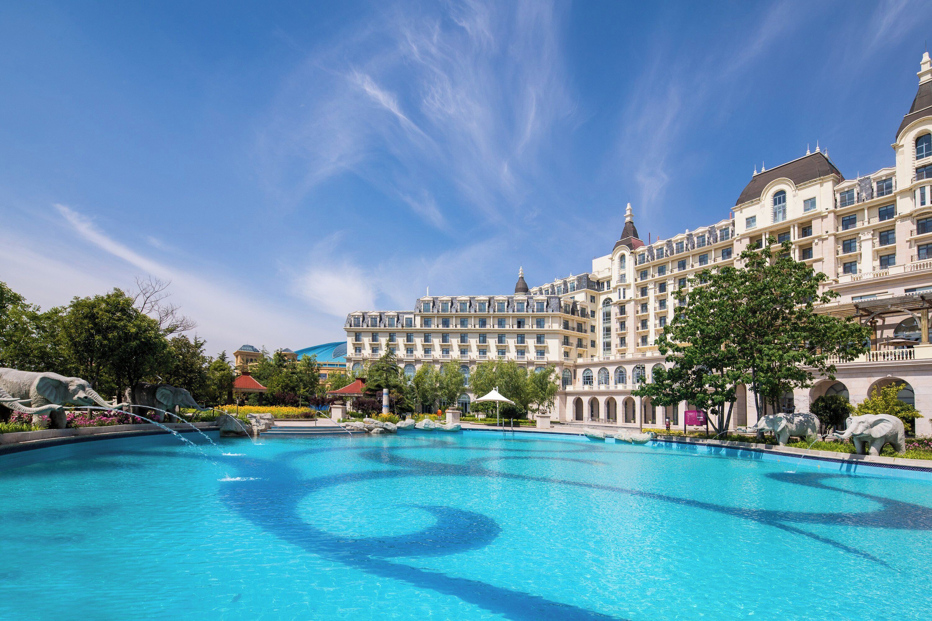 Um hotel grande com piscina, várias varandas e céu azul.