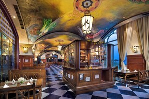 A hotel lobby with a checkered floor, a bar area, and a ceiling with a mural.