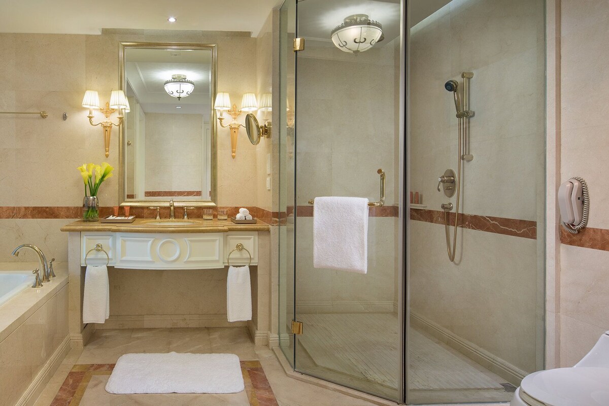 A bathroom with a bathtub, a glass-enclosed shower, a vanity with a mirror, and a vase of flowers.