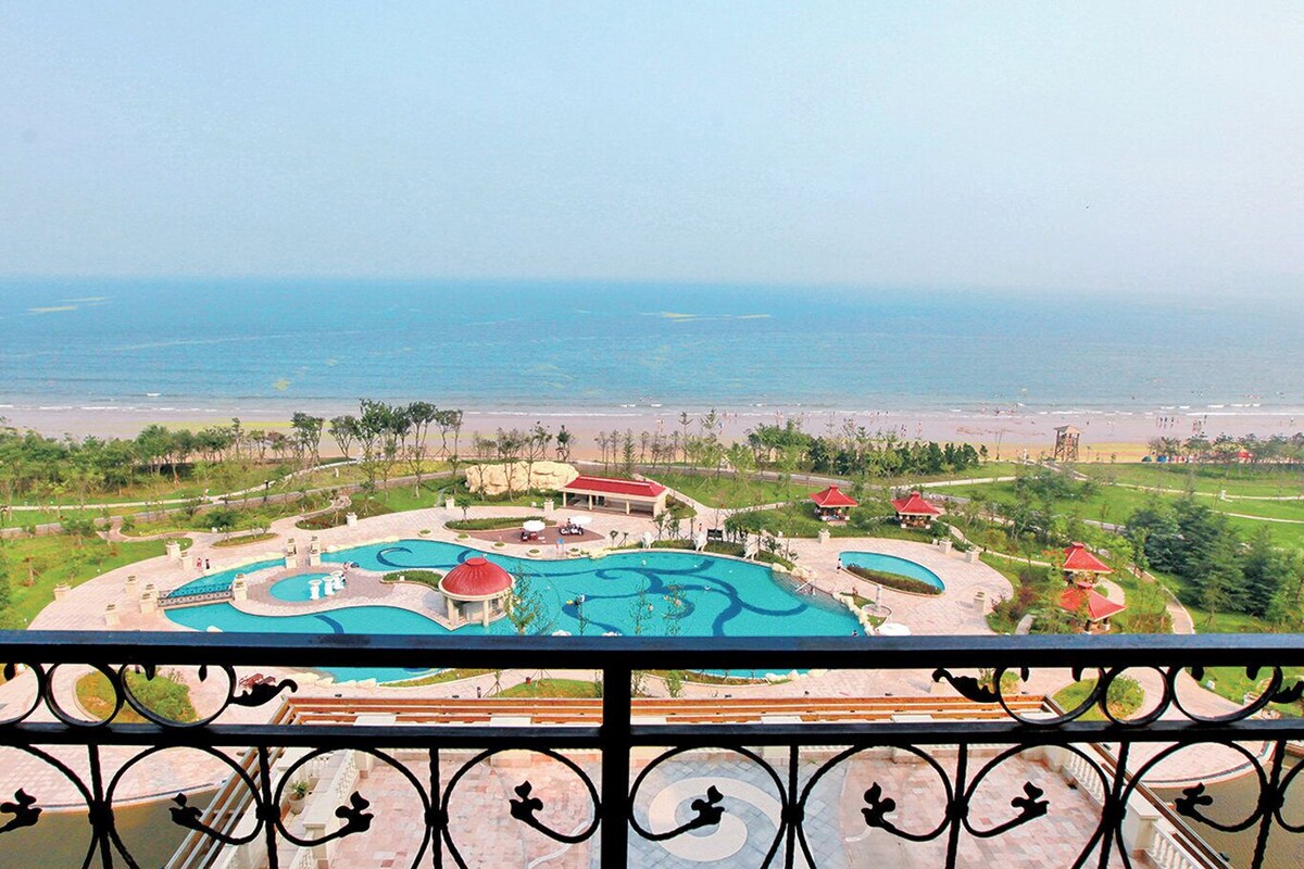 A resort with a large swimming pool, a beach, and a view of the sea.