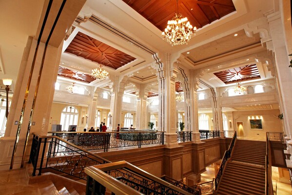 Un lobby espacioso con techos altos, columnas decorativas y una escalera central.
