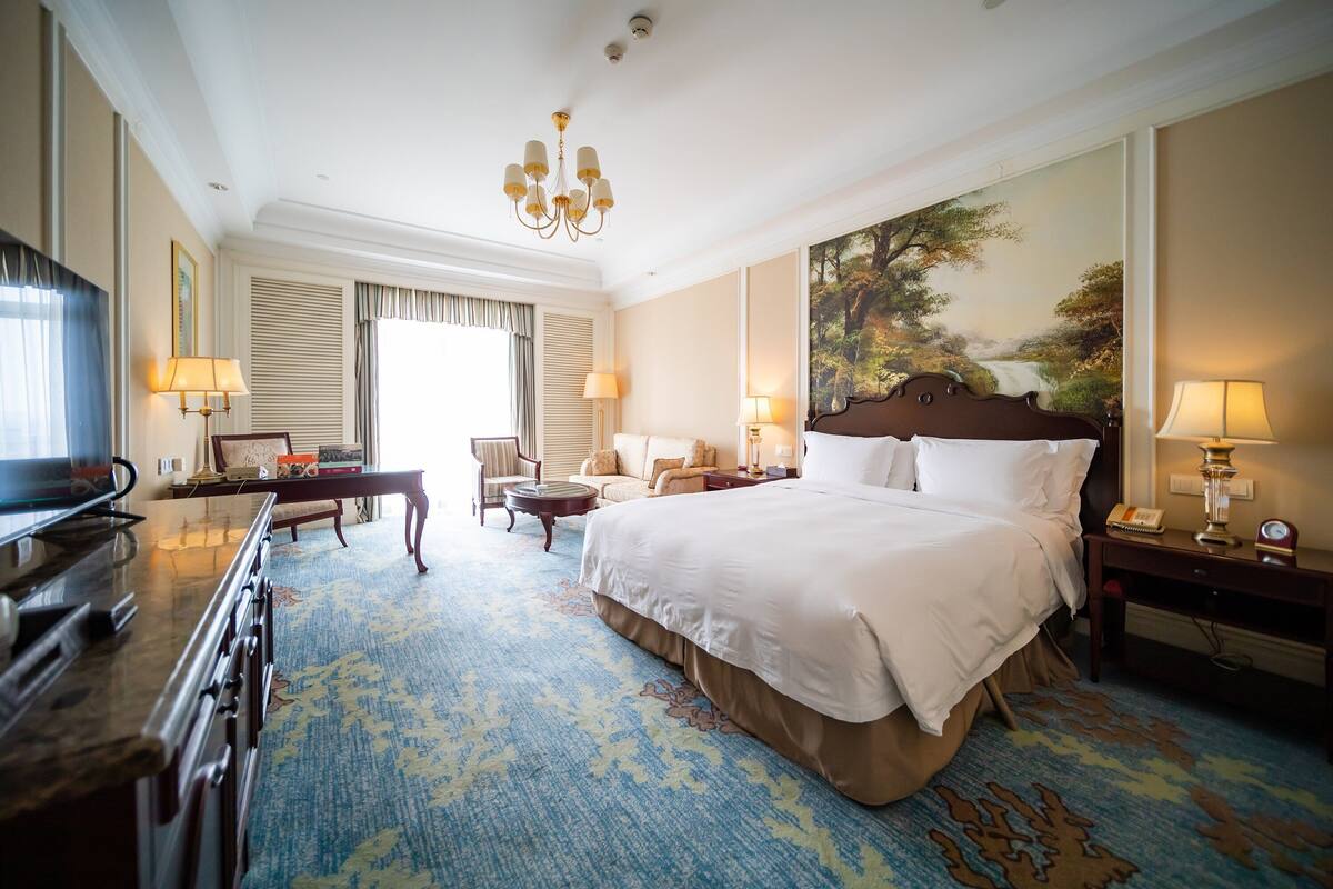 A hotel room with a large bed, a television, a desk, and a painting on the wall.