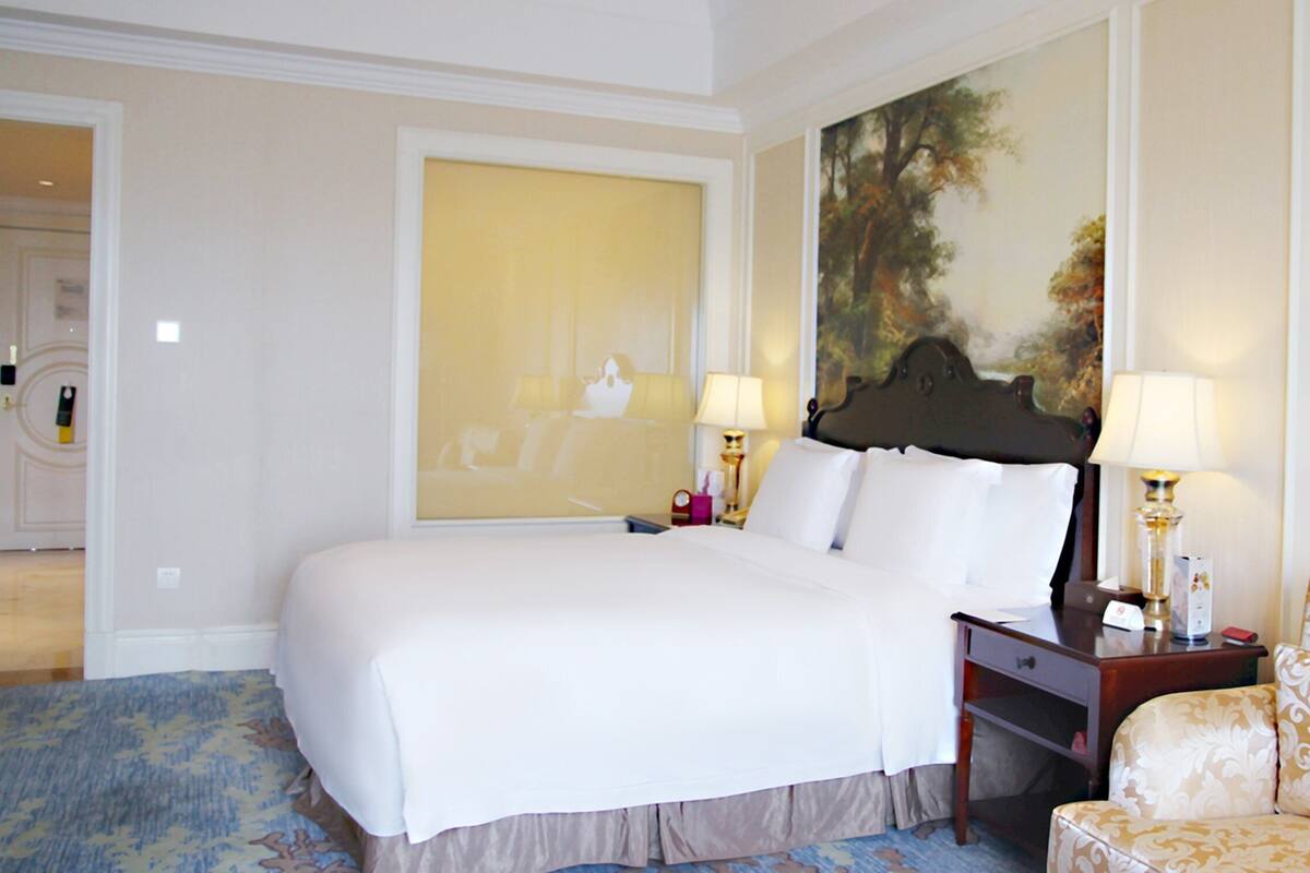 A hotel room with a large bed, two bedside tables with lamps, a sofa, and a large painting on the wall.