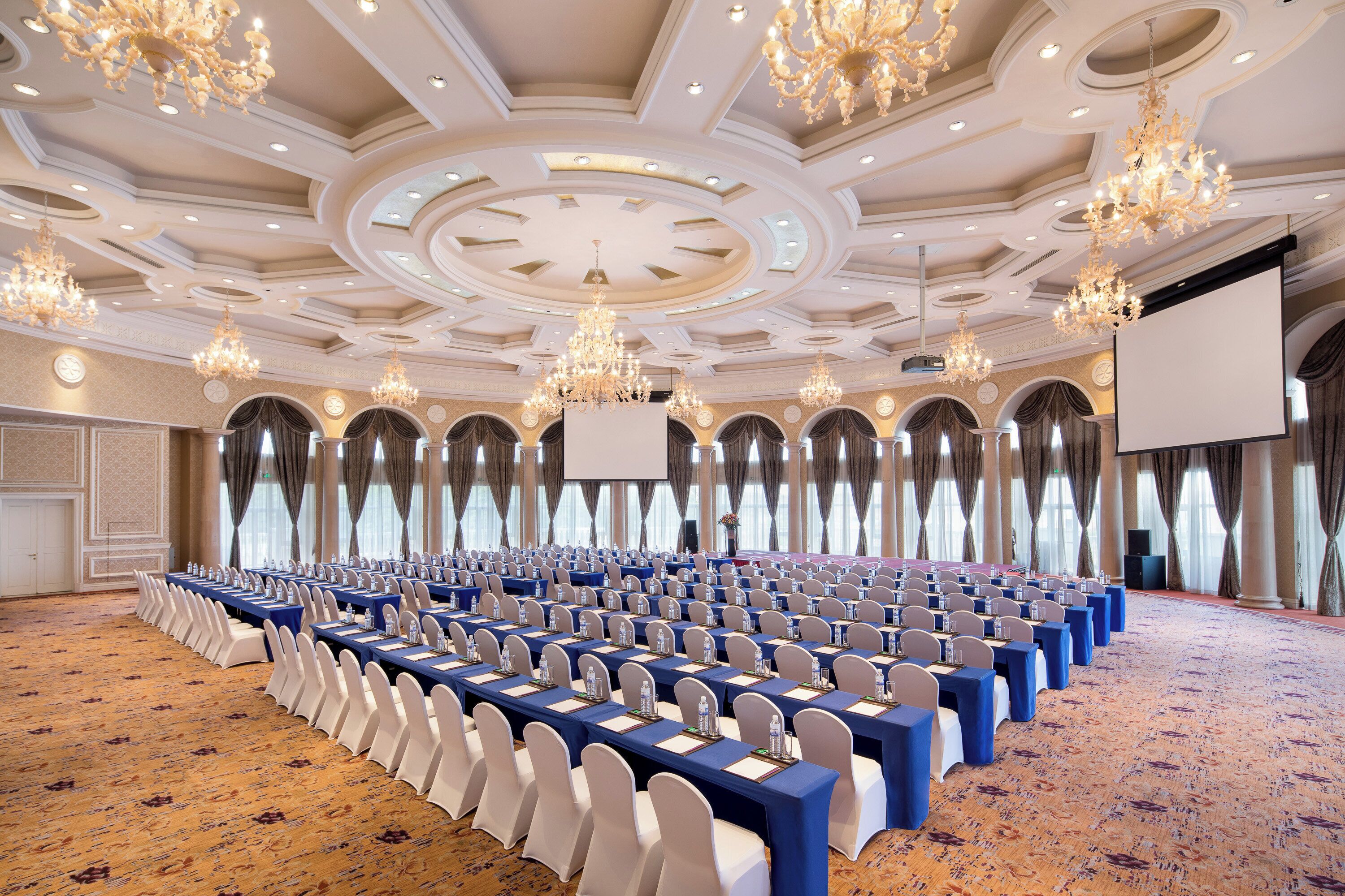 A conference room with rows of tables, chairs, and a large screen.
