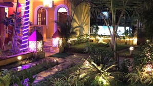 A well-lit building with a balcony, surrounded by lush greenery and decorative lighting. - Veronica Guest House (Calangute)