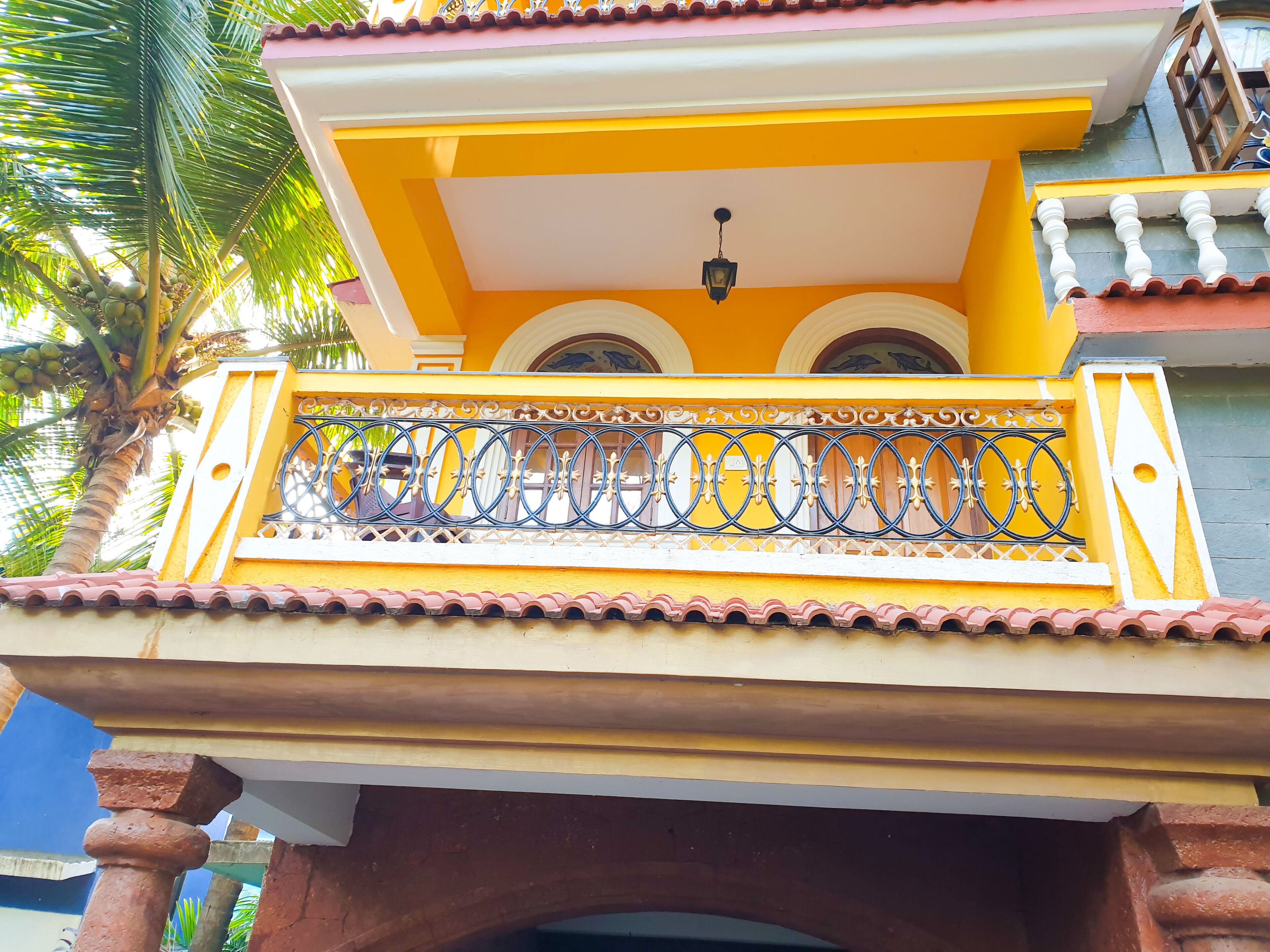 A yellow building with a balcony, a palm tree, and a tiled roof.