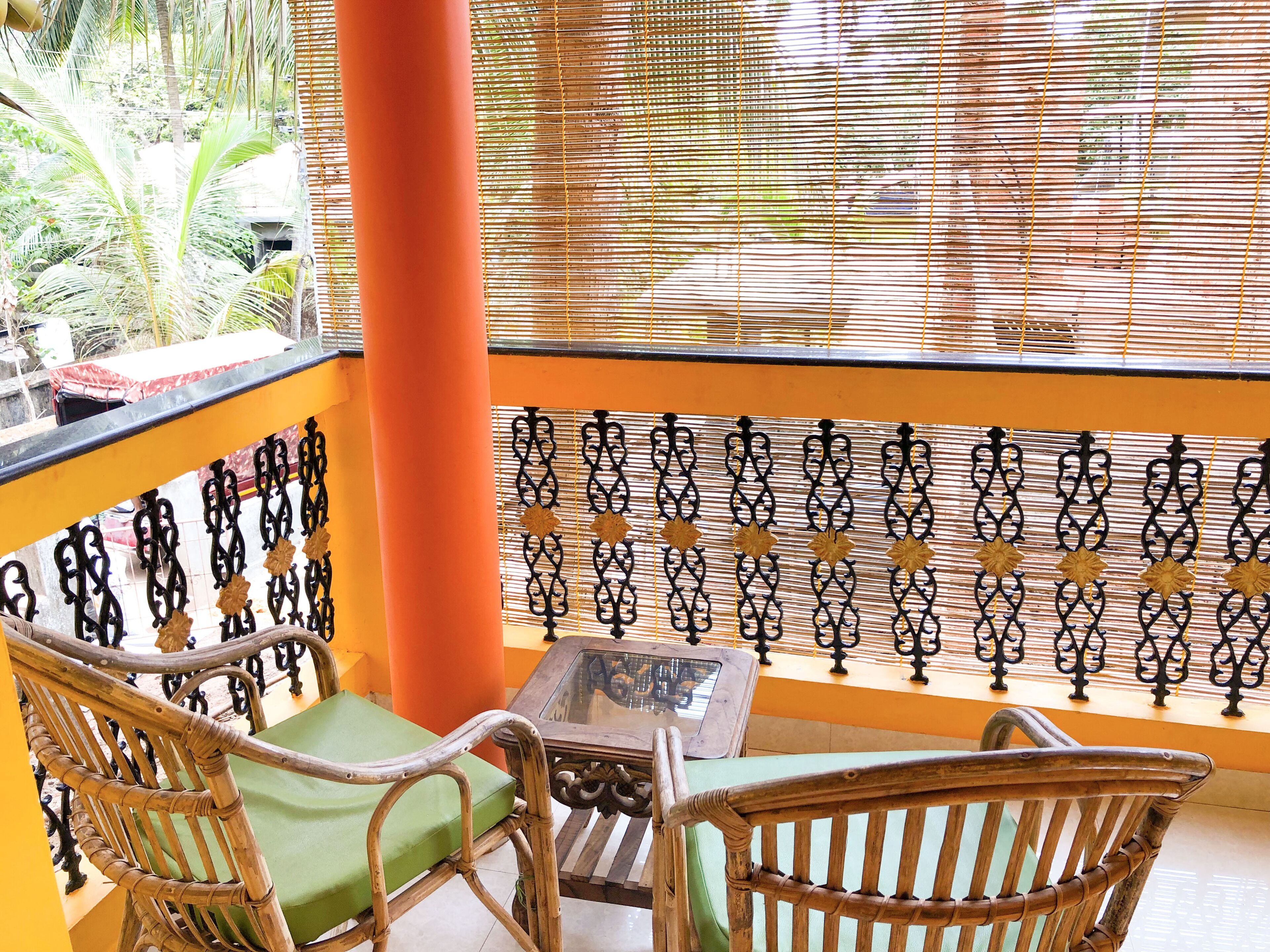 A balcony with wicker furniture, a glass table, and a view through a patterned bamboo blind.