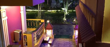 Una escalera conduce a un balcón con vistas a un jardín ajardinado de noche.