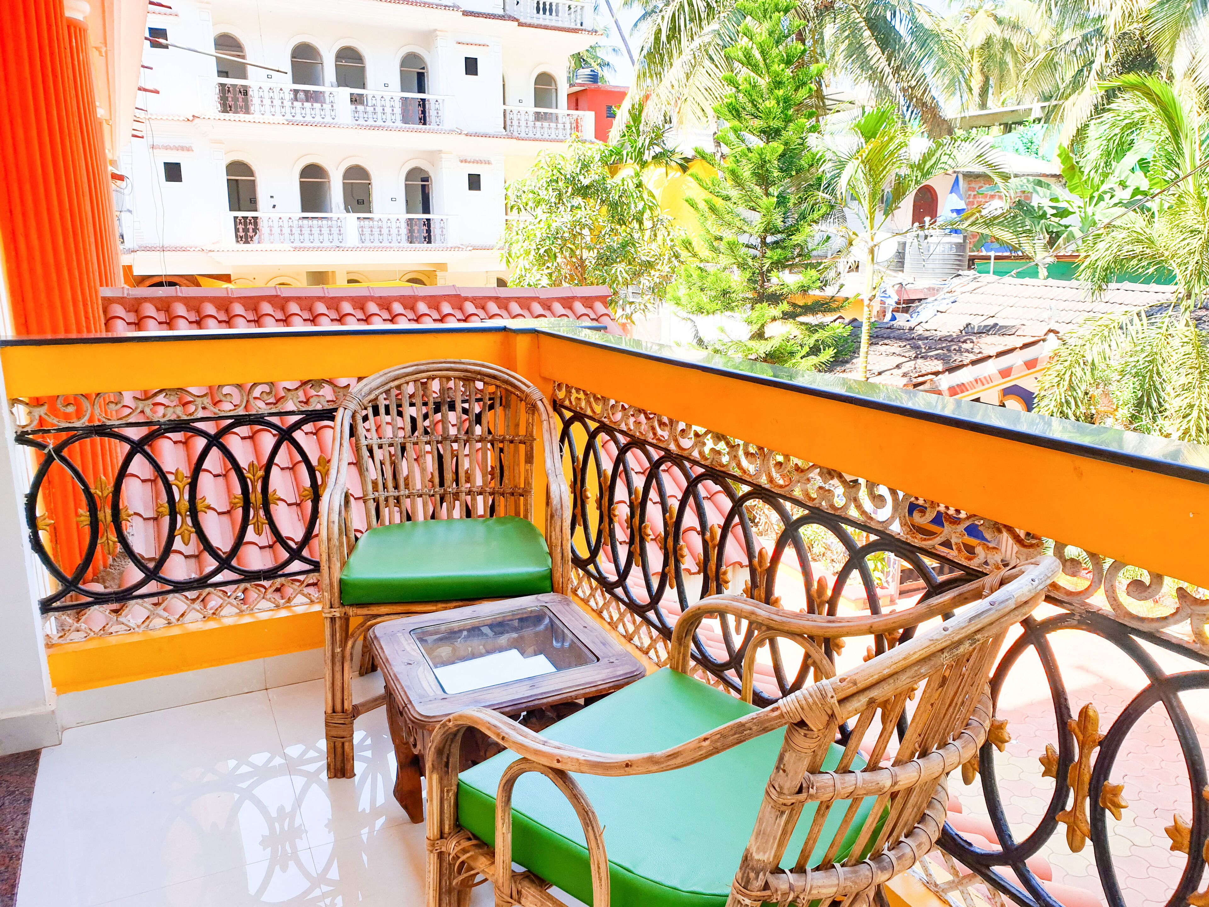 A balcony with wicker furniture, a glass table, and a view of a building and greenery.