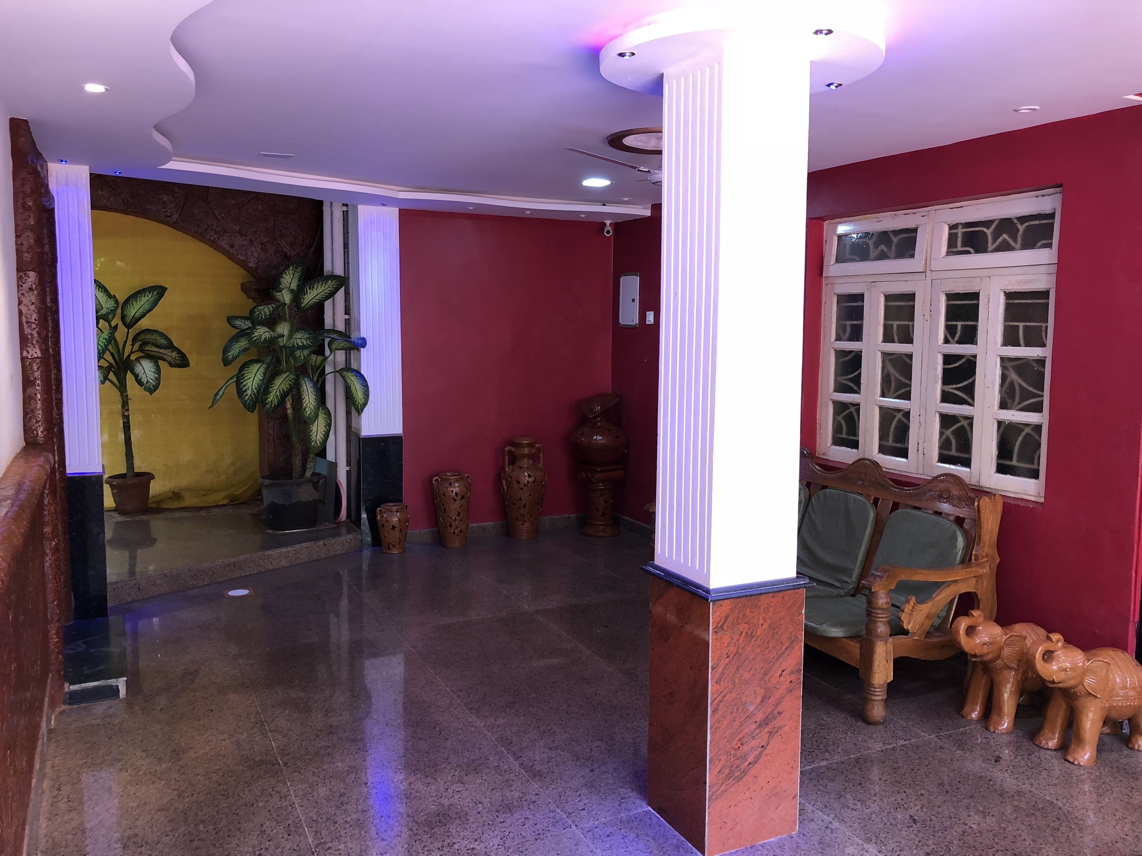 A lobby with a marble floor, a wooden bench with elephant sculptures, and a large window with patterned glass.