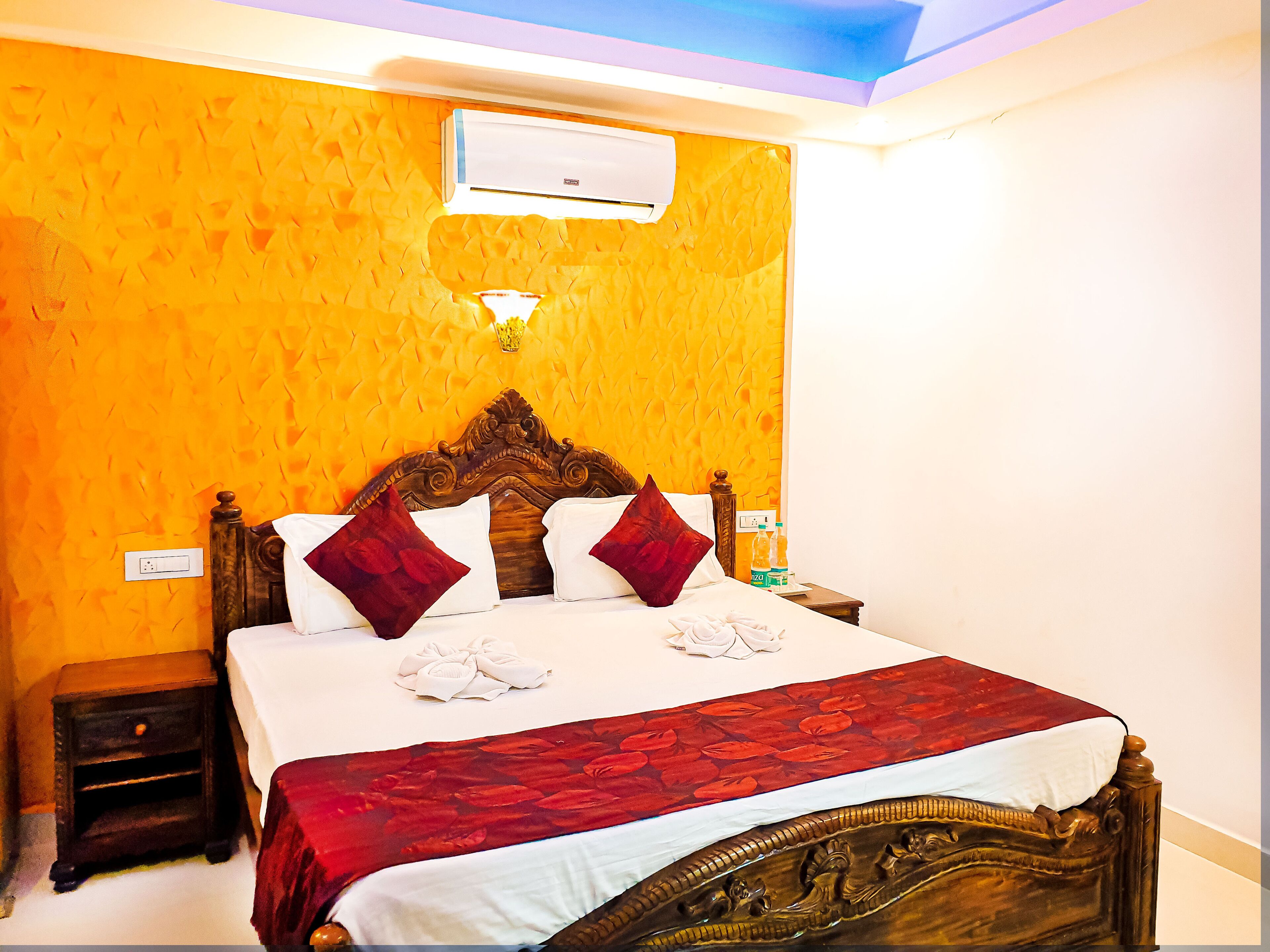 A hotel room with a wooden bed, red and white bedding, a small bedside table, and an air conditioning unit on the wall.