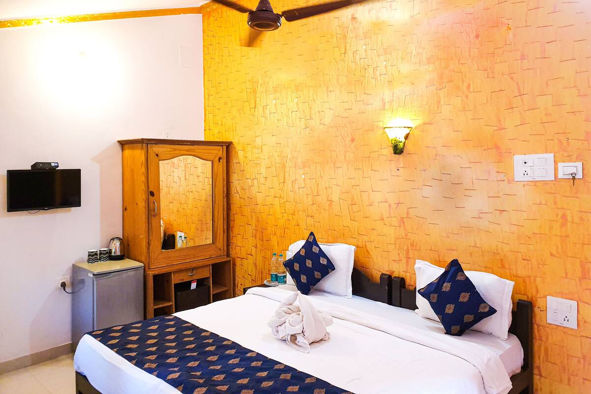 A hotel room with a bed, a ceiling fan, a TV, a wardrobe, and a wall-mounted light.