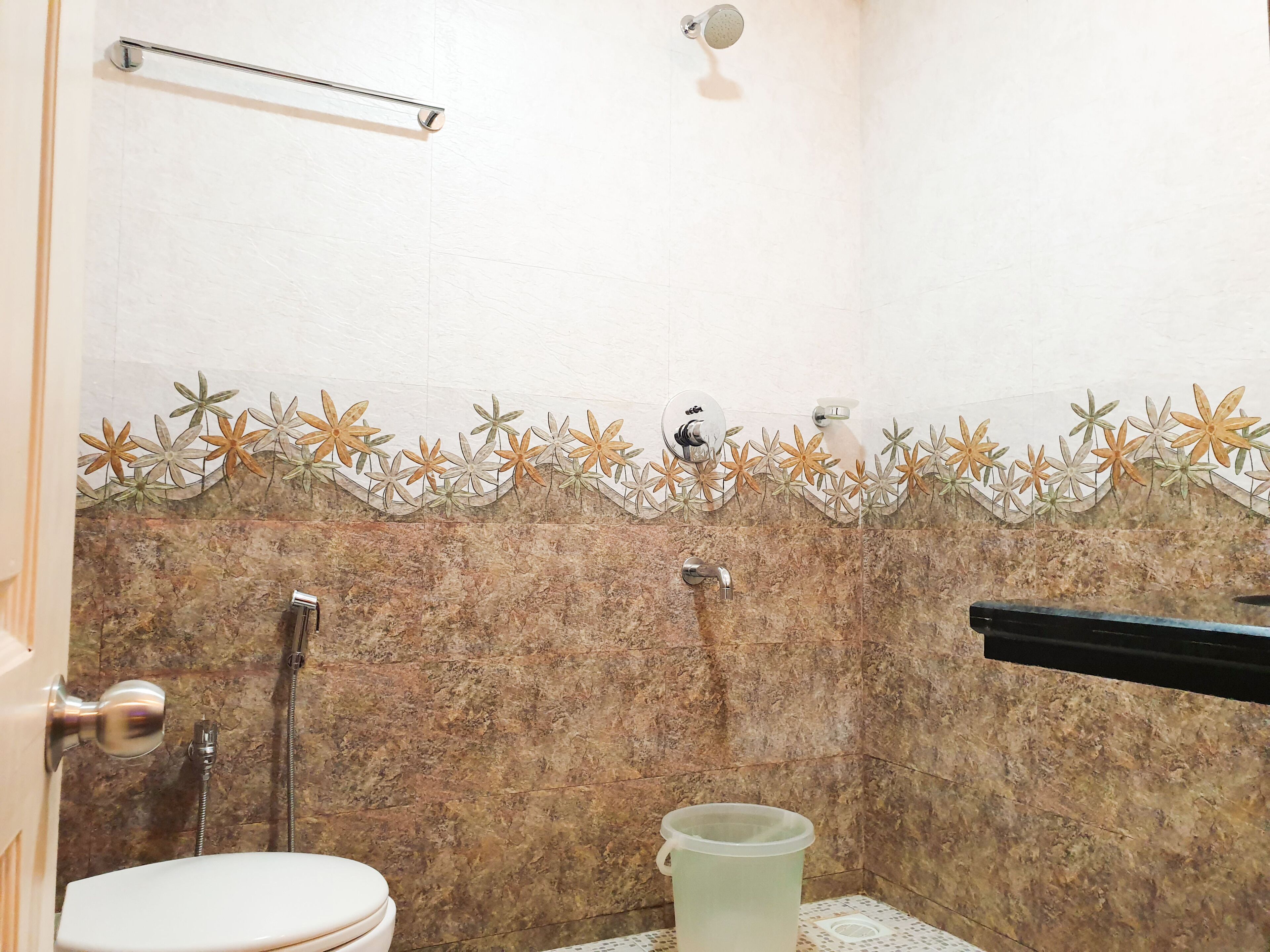 Un baño con inodoro, ducha y un detalle decorativo de azulejos con motivos florales.
