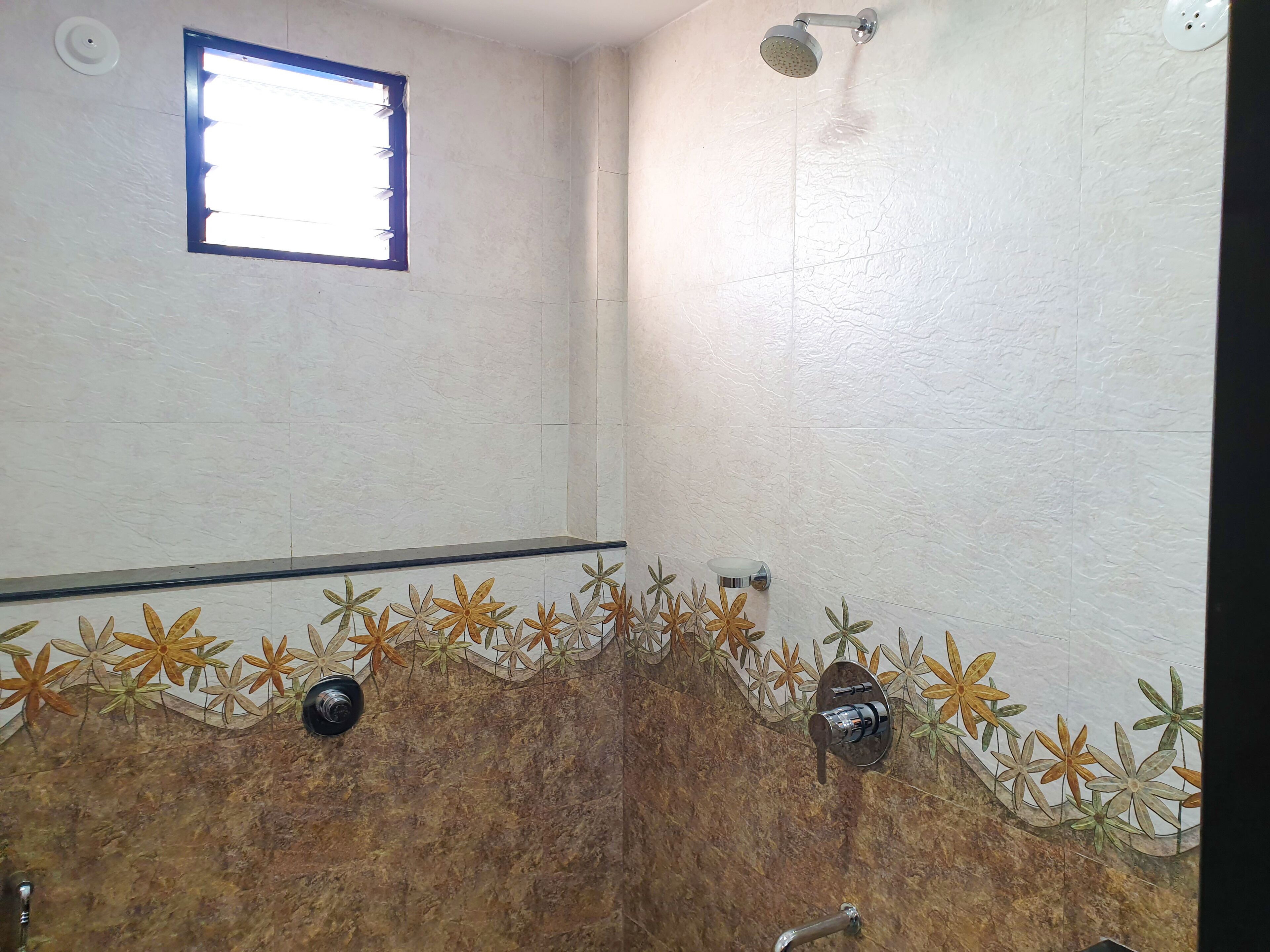 Une salle de bain avec une douche, une fenêtre et une bordure décorative en carreaux.