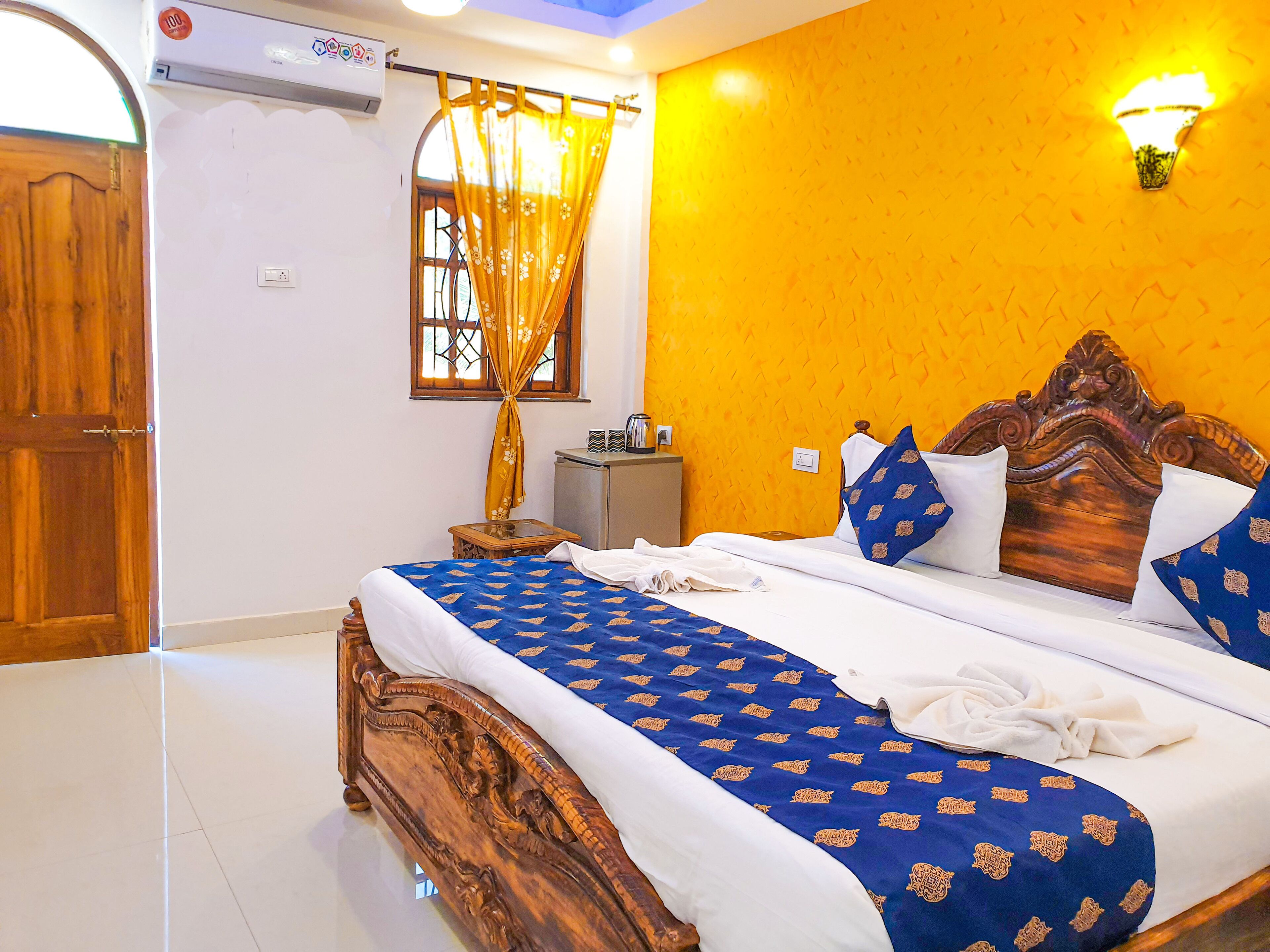 A hotel room with a wooden bed, a yellow accent wall, and a window with a curtain.