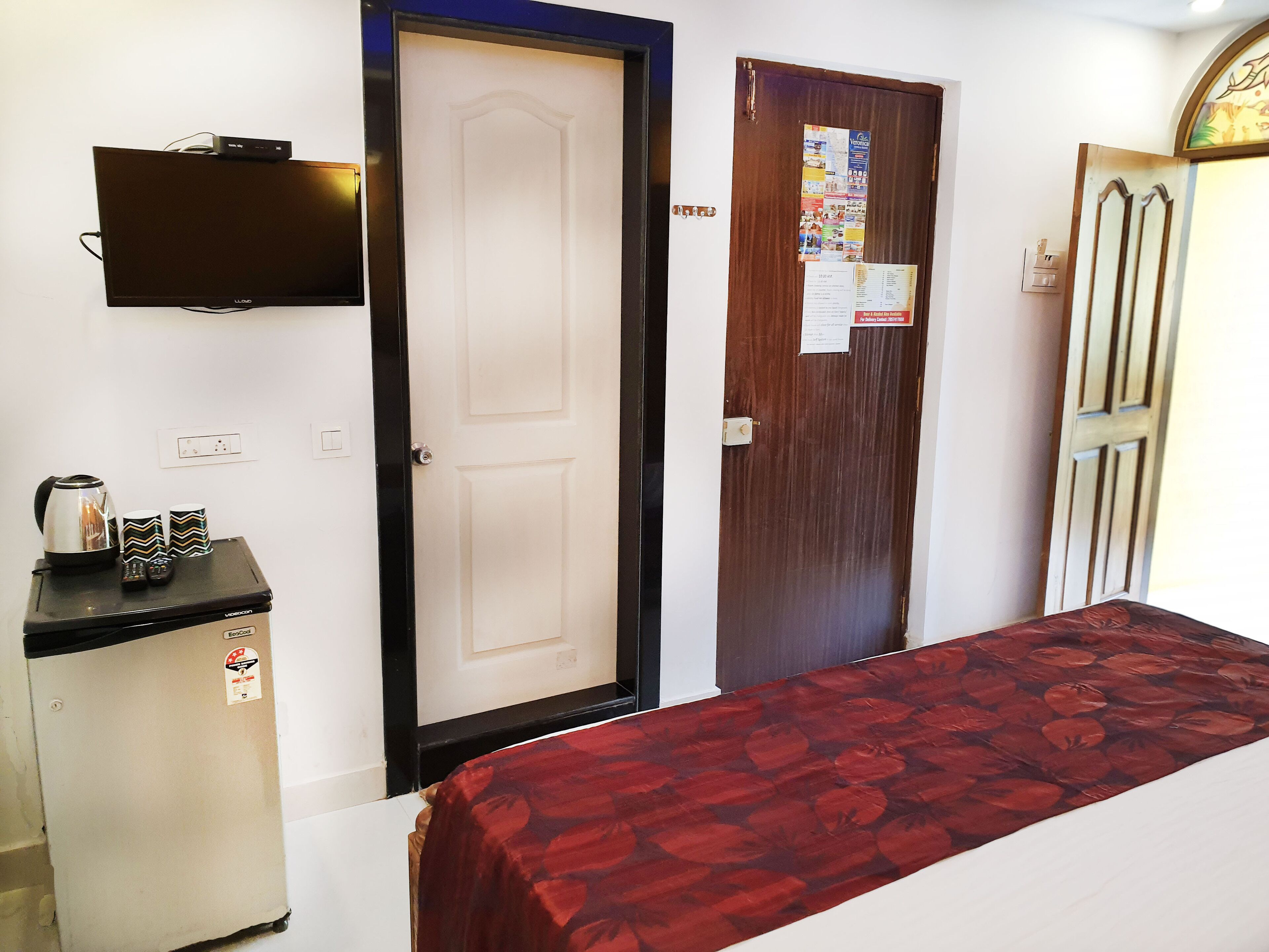 Una habitación con cama, un refrigerador pequeño, un televisor montado en la pared y una puerta con un cartel.