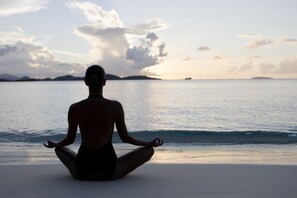 A person meditating on a beach with a view of the ocean and distant islands.