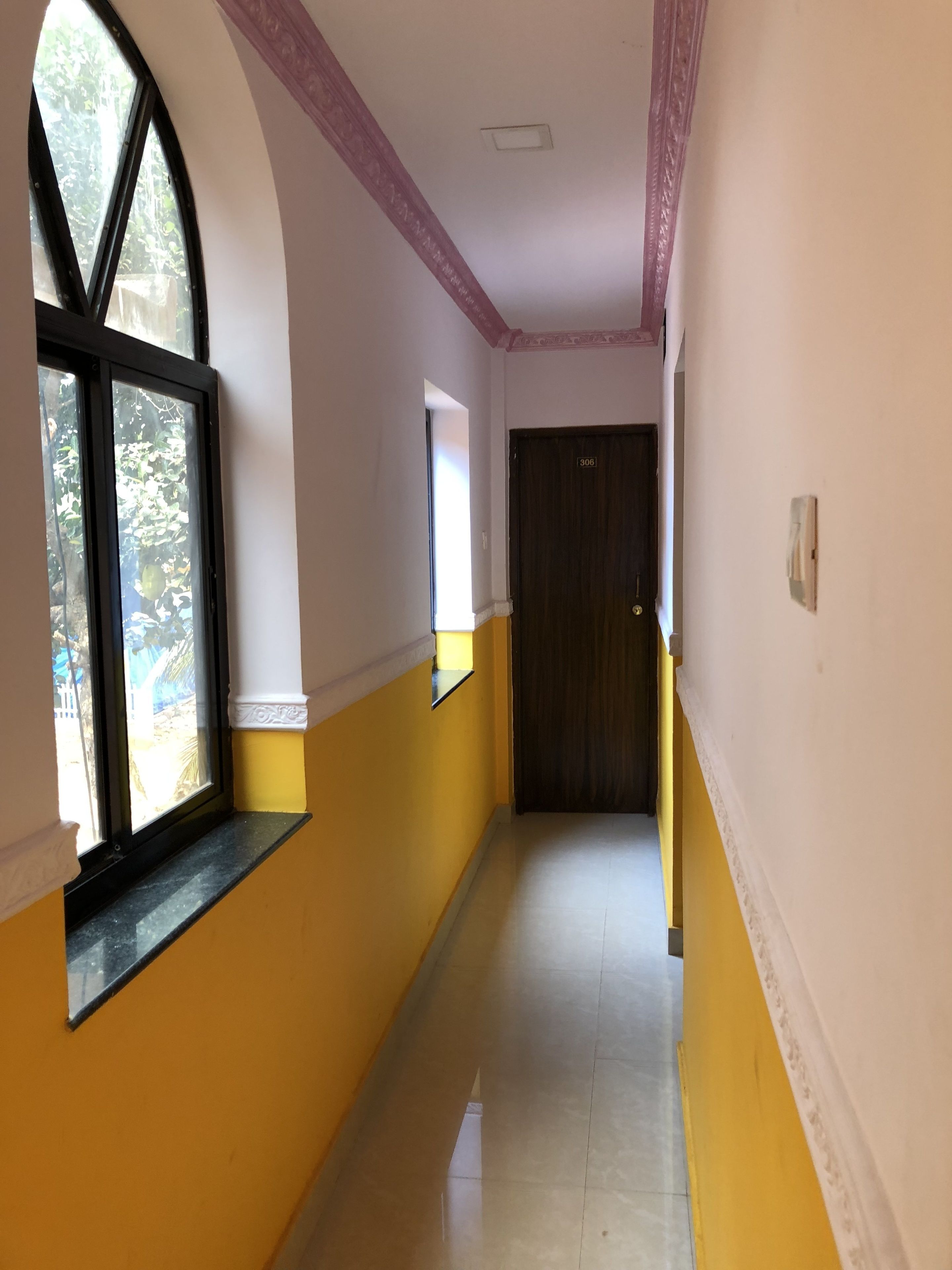 A corridor with a yellow and white color scheme, a large arched window, and a door with the number 306.