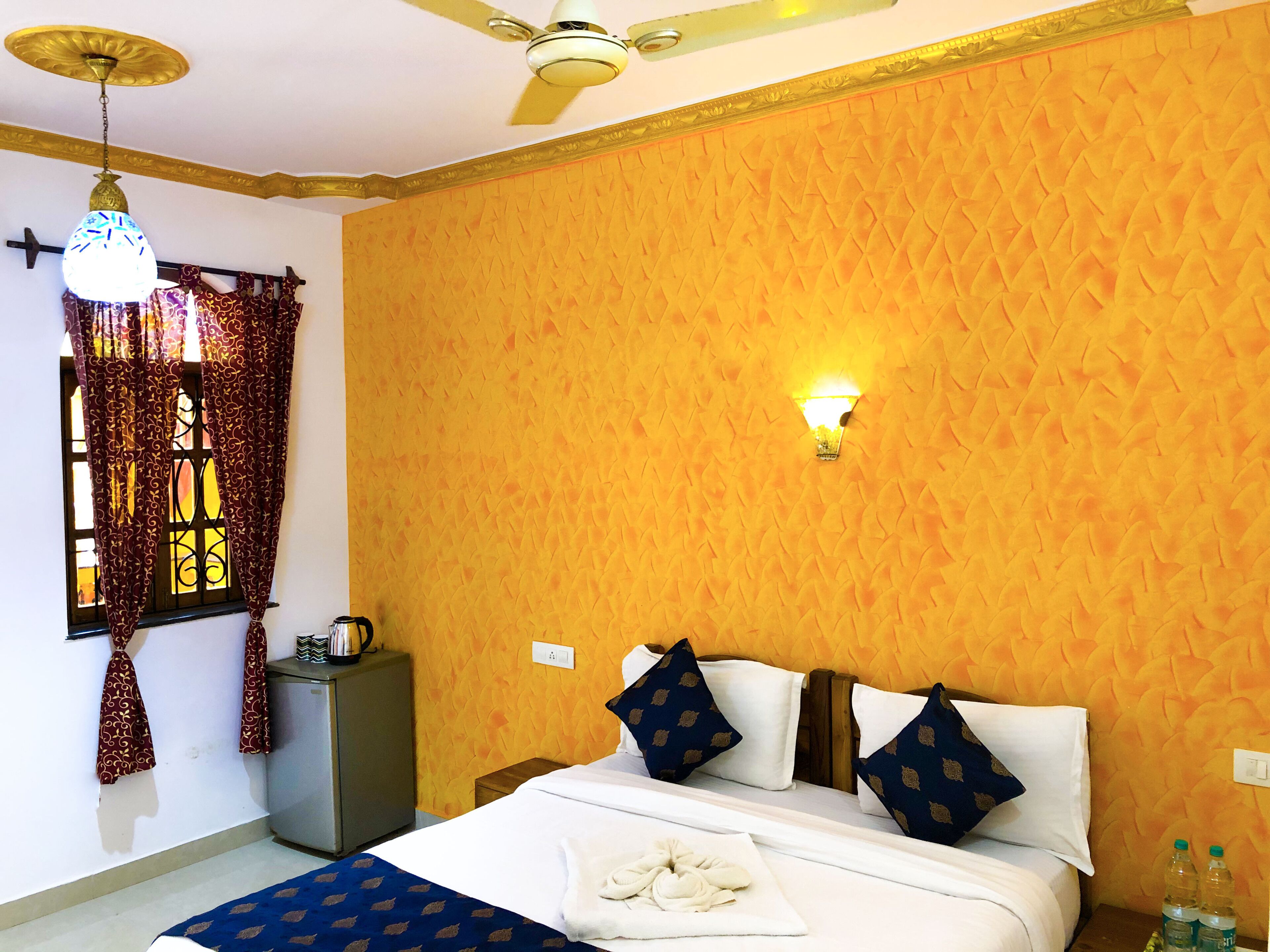 A hotel room with a bed, a ceiling fan, a window with curtains, a nightstand, and a wall-mounted light.