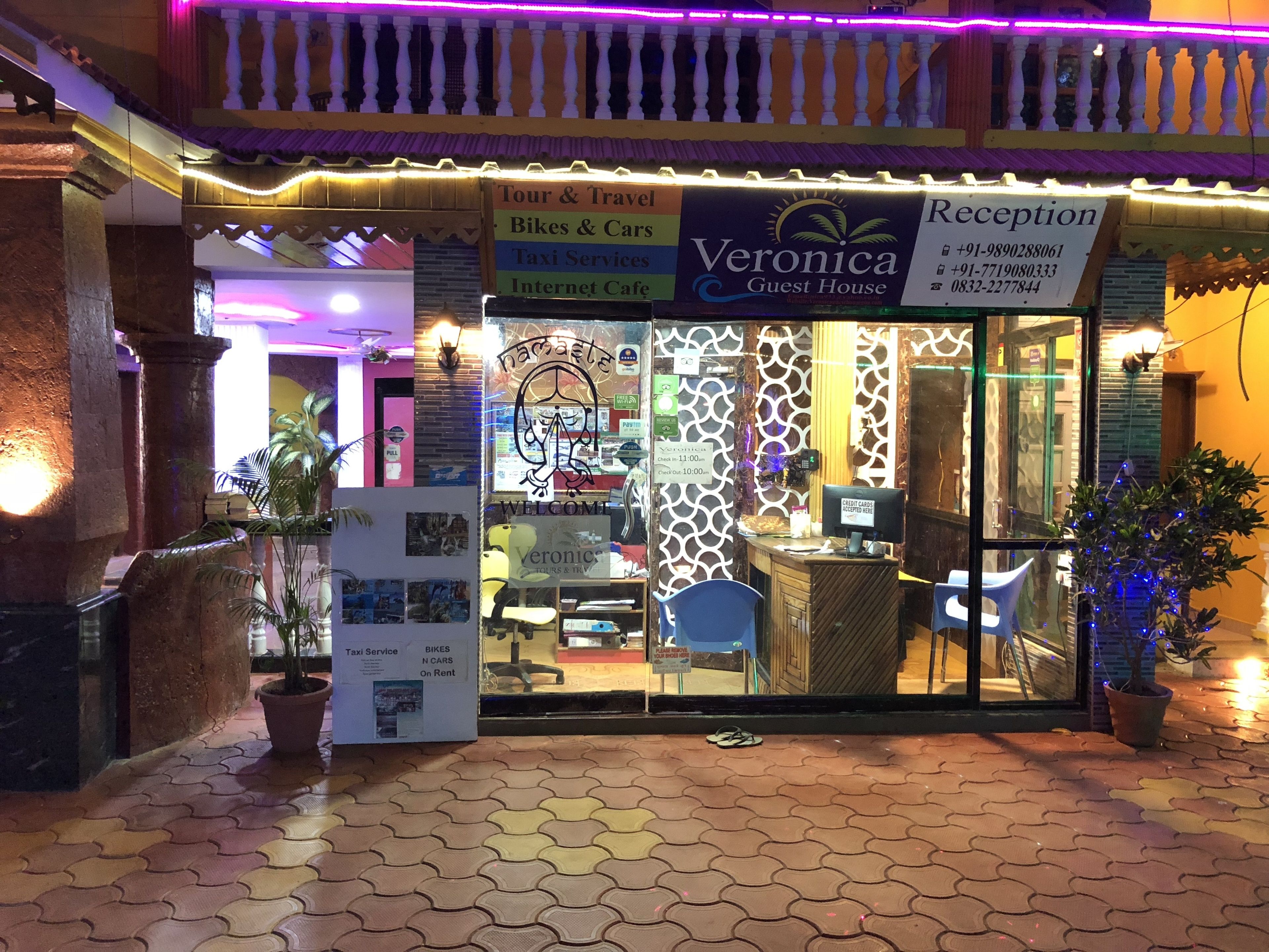 A guest house named Veronica with a reception area, reception desk, and a signboard for Tour & Travel, Bikes & Cars, Taxi Services, and Internet Cafe.
