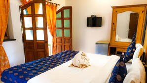 A neatly made bed with a blue patterned bedspread and white linens, a wooden wardrobe with a mirror, and a small bedside table with a lamp. - Veronica Guest House (Calangute)