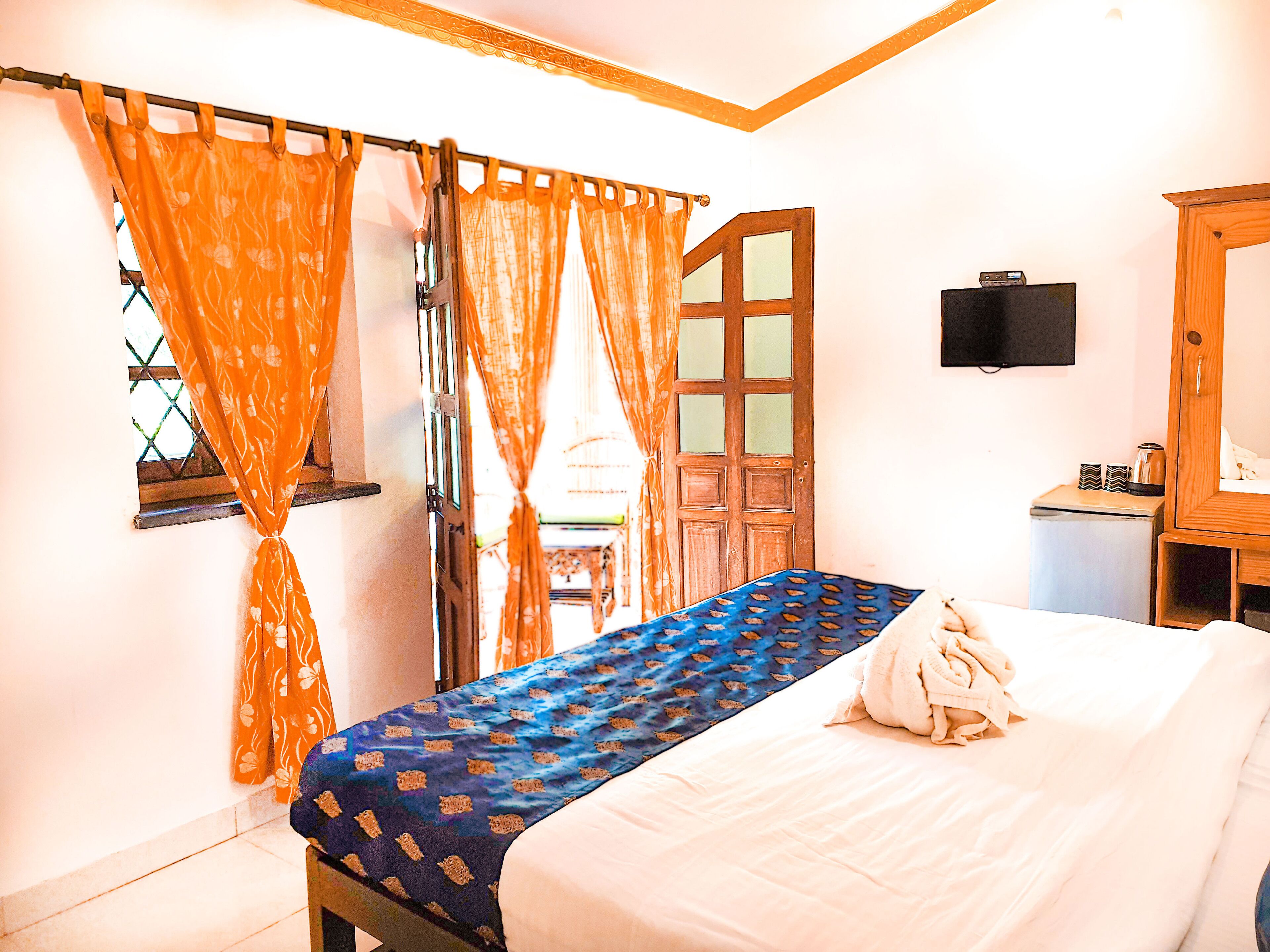 A bedroom with a bed, curtains, a television, and a small table with items on it.